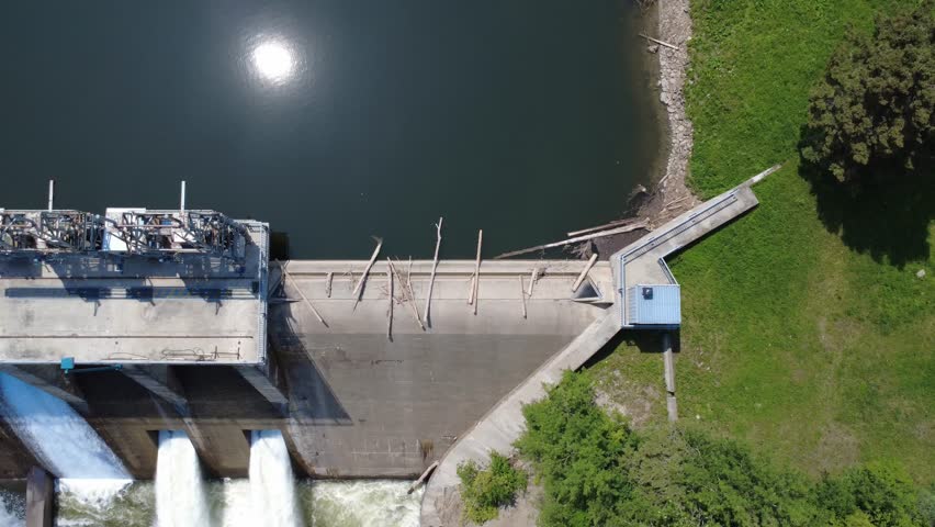 Aerial view of a hydroelectric dam structure with its spillway gates in operation, creating jets and cascades of water with the sun reflecting off the reservoir. Mitis-2, Price, Quebec, Canada.