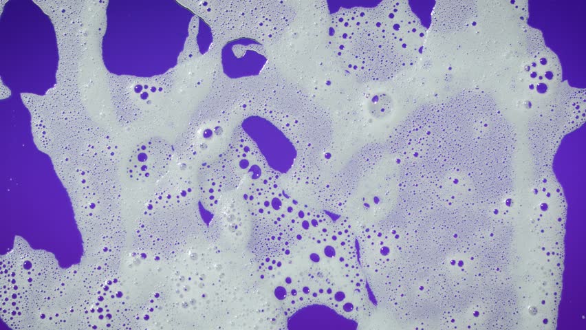 White soap foam bubbles gently move across a purple background in slow motion, creating a clean and calming aesthetic — perfect for hygiene, skincare, spa, product promos, and wellness visuals.
