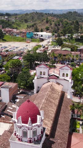 Aerial view of the red dome and bell towers of Our Lady of Carmen Church in Guatape, Colombia, surrounded by traditional tiled roofs. Vertical Video
