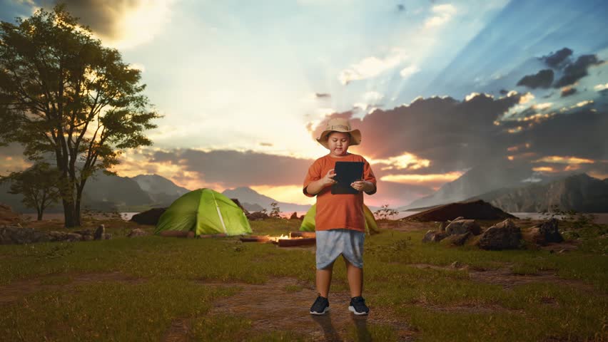 Asian Boy With A Hat Smiling And Pointing To A Tablet While Tent Camp Lakeside. Boy Researcher Examines Something, Travel Tourism Adventure Concept, Full Body