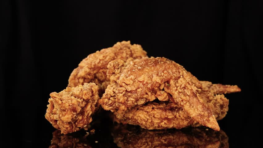 Close-up sequence of hands tearing apart a crispy fried chicken wing on a glossy black surface, under bright, even lighting with minimal camera movement