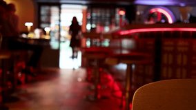A silhouetted woman enters a contemporary bar with red neon accents, captured in soft focus with moody, low ambient lighting and a stationary camera - Powered by Shutterstock - Get 15% off with code: PIKWIZARD15