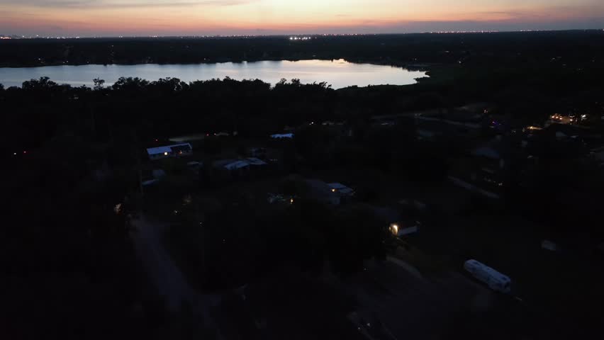 Dark neighborhood in Florida and lake during golden sunset at horizon. Aerial top down flyover. Cars on Main Street. dark residential area in plant city, Florida.