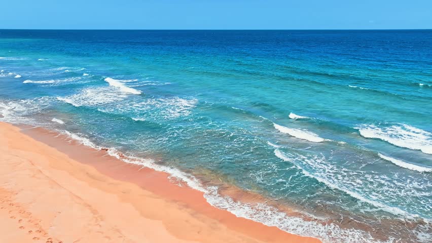 Blue wave view on tropical paradise beach of Pacific ocean. Sea waves on golden sand. Clear sunny day over green sea waters. Waves crashing on sandy beach. Changeable windy weather.