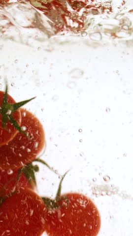 Vertical fresh red cherry tomatoes moving and splashing in water in slow motion