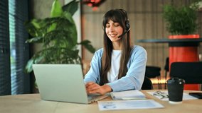 Professional businesswoman, dressed in a blue shirt, smiling and focused during an online video call in a modern office. She is actively engaged in virtual work, using a headset and laptop. - Powered by Shutterstock - Get 15% off with code: PIKWIZARD15
