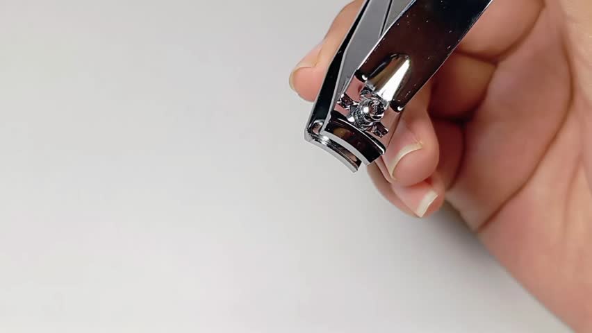 A person carefully uses a nail clipper to trim a fingernail, focusing on hygiene and neatness.