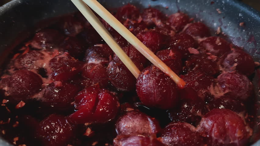 Juicy plum being lifted from thick syrup using chopsticks during cooking process.