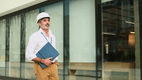 Confident architect wearing hardhat and holding blueprints is smiling in front of modern building - Powered by Shutterstock - Get 15% off with code: PIKWIZARD15