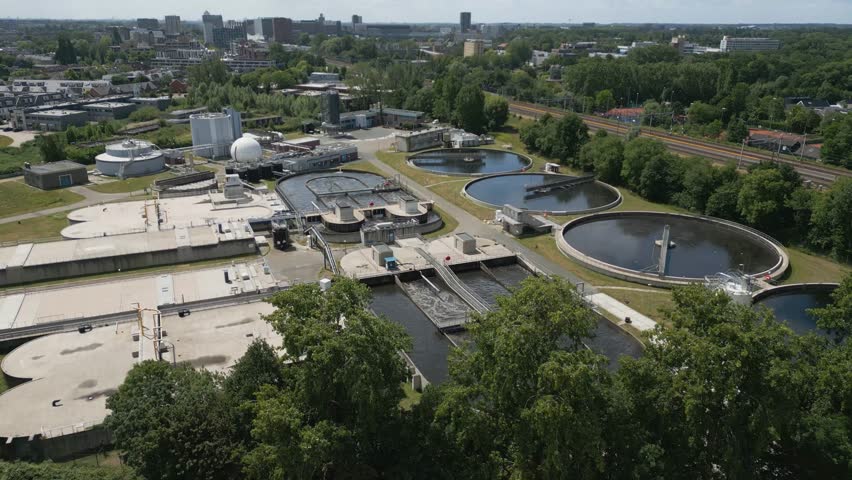 Top-down drone shot of a large modern water treatment facility in Leiden, surrounded by urban landscape and train infrastructure.