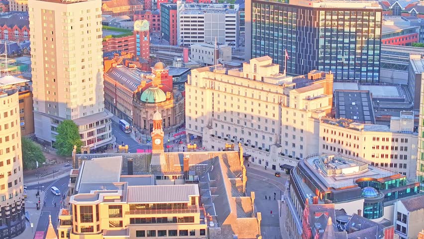 Drone shot over Park Square in Leeds, UK, showcasing classic and modern buildings illuminated by warm golden hour light in the urban core.