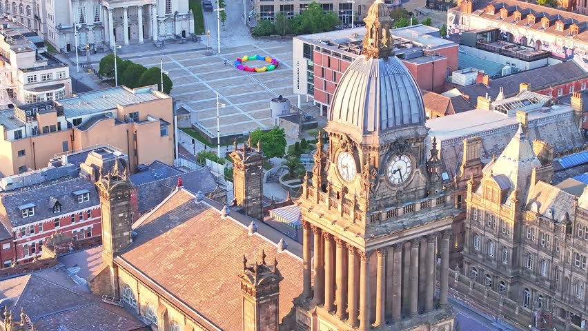 Drone ascending shot over Leeds Town Hall revealing its iconic dome and Millennium Square beyond, bathed in soft early morning light in central Leeds, UK.