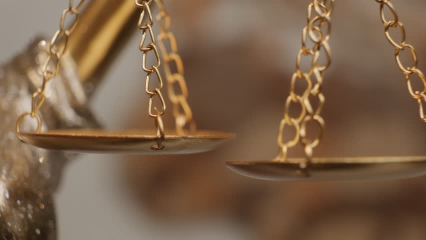 Golden scales of Justice Statue swaying on abstract background as symbol of weighing good and evil, guilt and innocence close-up