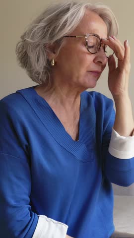 Senior woman suffering from vertigo, migraine or headache in slow motion. Elderly woman feeling dizziness, taking off glasses, touching face and head