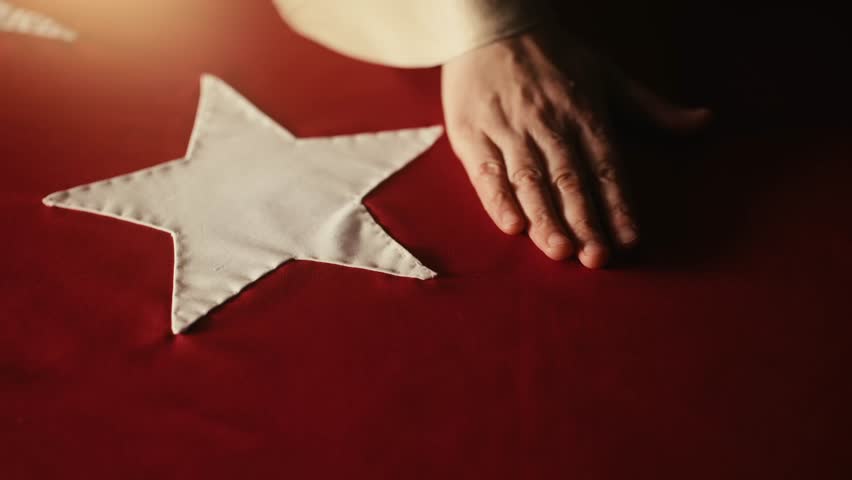 A veiled woman sewing the Turkish flag with a needle and thread