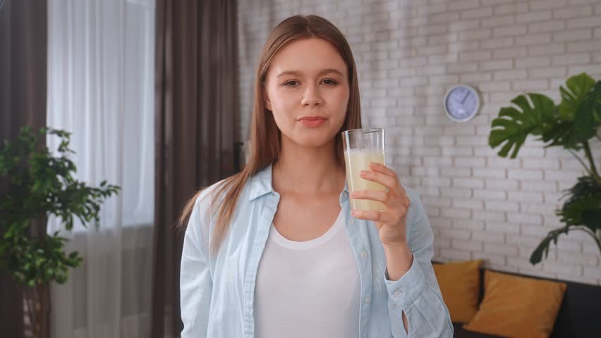 A young woman cracks collagen powder in a glass of water with a teaspoon and takes a sip. The concept of healthy living and self care, beauty .