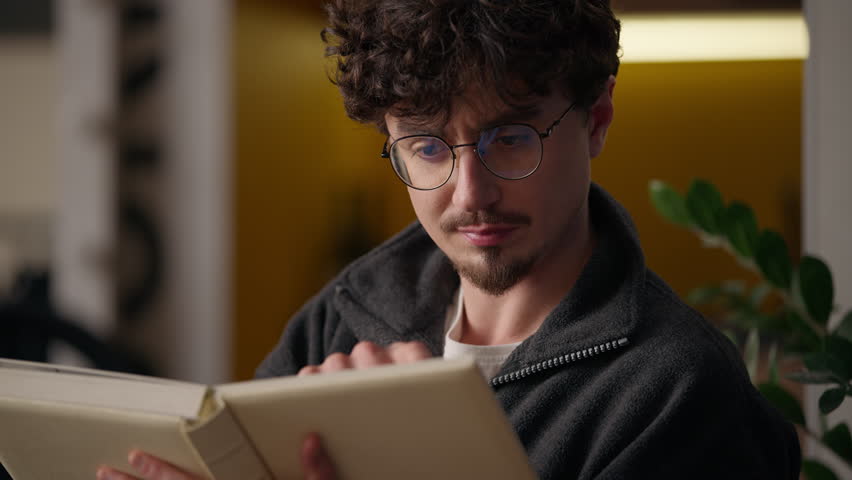 Pensive serious Caucasian hipster guy thinking reading book at home male reader man read classic literature novel pages studying indoors smart learner pondering looking interesting story text learning