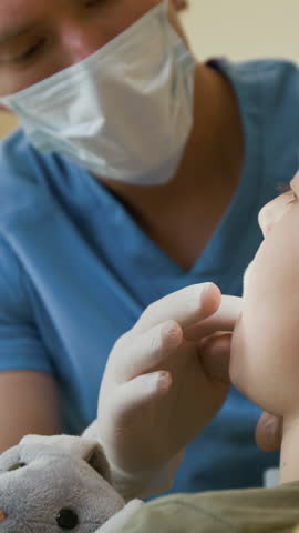 Vertical shot of young child sitting in dental chair with dentist carefully performing teeth and gum exam