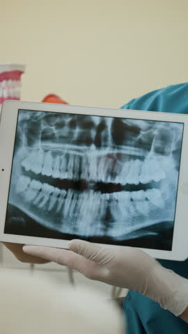 Vertical shot of young woman as dentist holding tablet with dental x ray image on screen and showing to patient
