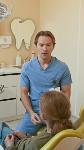 Vertical shot of pediatric dentist consulting unrecognizable child sitting in dental chair and taking tooth model for demonstration