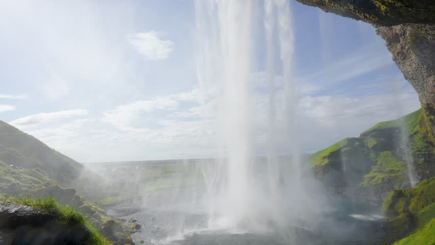 Vibrant Seljalandsfoss Waterfall flows down green cliffs under a clear blue sky in Iceland spring with tourists nearby.