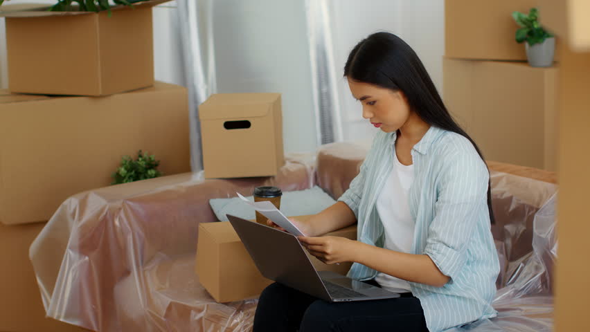 Asian woman relocating to a new apartment with boxes and technology in use