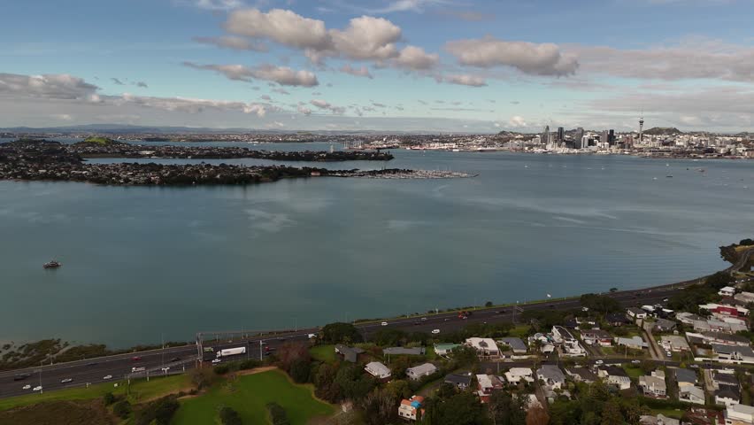 Aerial view of traffic on motorway alongside Shoal Bay, Auckland skyline and Sky Tower in distance. New Zealand