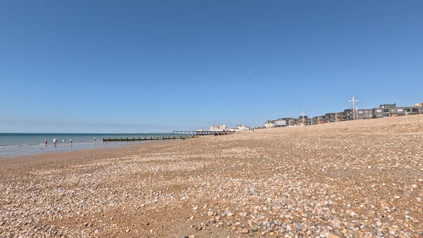 Pebble beach along the English Channel with wooden groynes and seaside buildings under a clear blue sky. Calm shoreline and relaxed coastal atmosphere. Submitted for the sstkTravel contest.