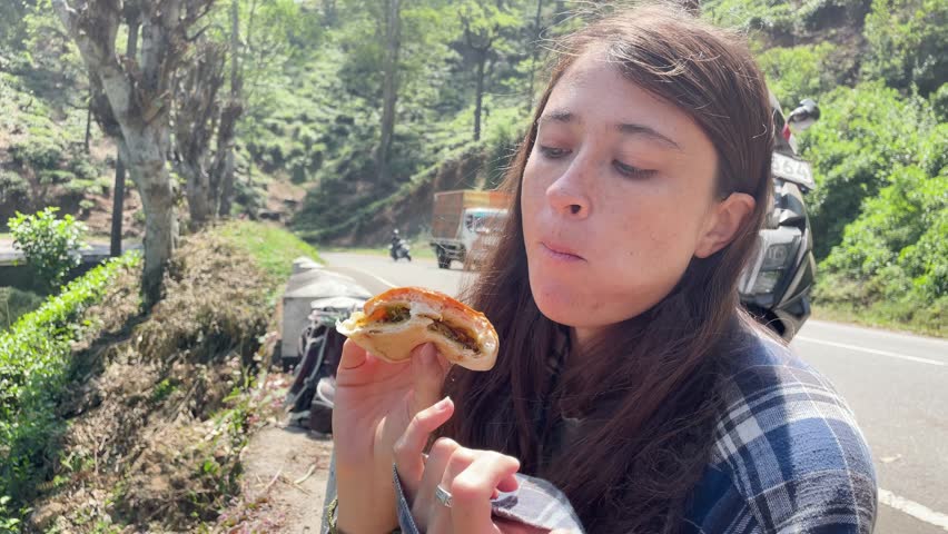 Young woman eating freshly baked Sri Lankan snacks while sitting on the roadside. Authentic street food experience and local culture in Ella, Sri Lanka
