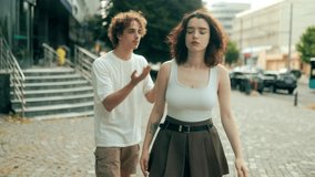 A curly-haired man kneels on the street, pleading emotionally with his partner. She stands with hands on hips, looking frustrated. Real urban couple moment outdoors. - Powered by Shutterstock - Get 15% off with code: PIKWIZARD15