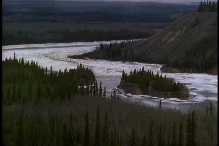 YUKON, ALASKA - CIRCA SEPTEMBER 1996: LS Icy water flowing in the Yukon river, surrounded by mountains and evergreen trees. Camera follows river.