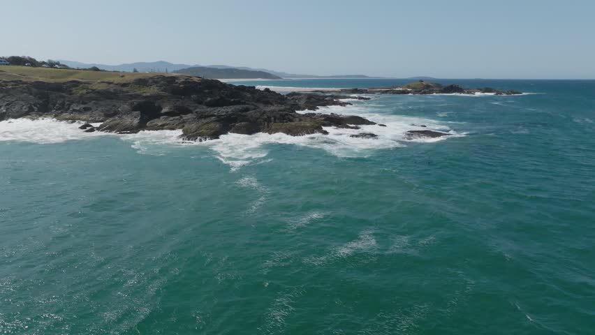 Drone aerial clip showing waves crashing onto rocky shoreline and pod of dolphins swimming close to rocks