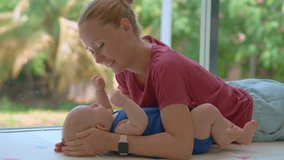 Young mother lies on the floor by a large window with lush tropical greenery, kissing her 3-month-old son. Tender bonding moment, love, and early motherhood in a peaceful natural setting. Slowmotion - Powered by Shutterstock - Get 15% off with code: PIKWIZARD15