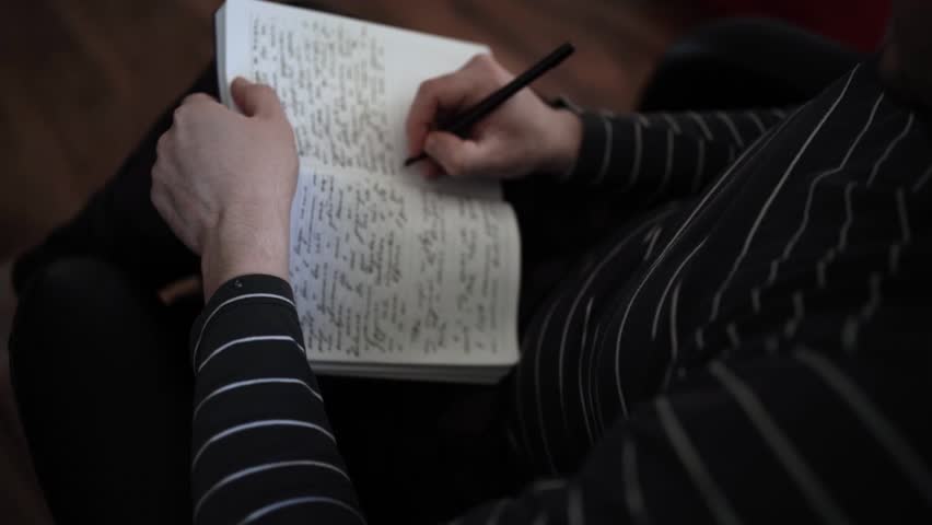 Close-Up of Person Writing in Notebook Wearing Striped Shirt, Seated