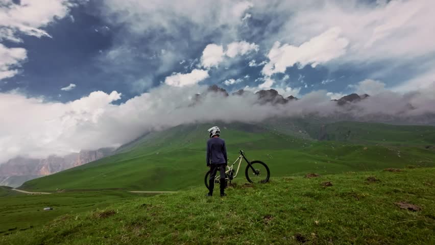 Young man getting on his bike in the mountains. Aerial view from fpv drone. Start of mtb downhill cycling rider