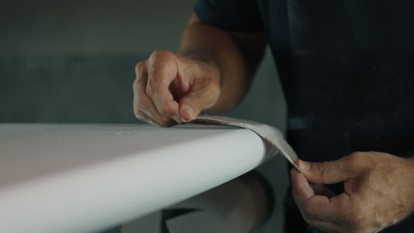 Surfing board shaper works on the surf board factory and creates a surf board. Brazilian shaper produces surfing board and polish it in the room on a surfboard factory