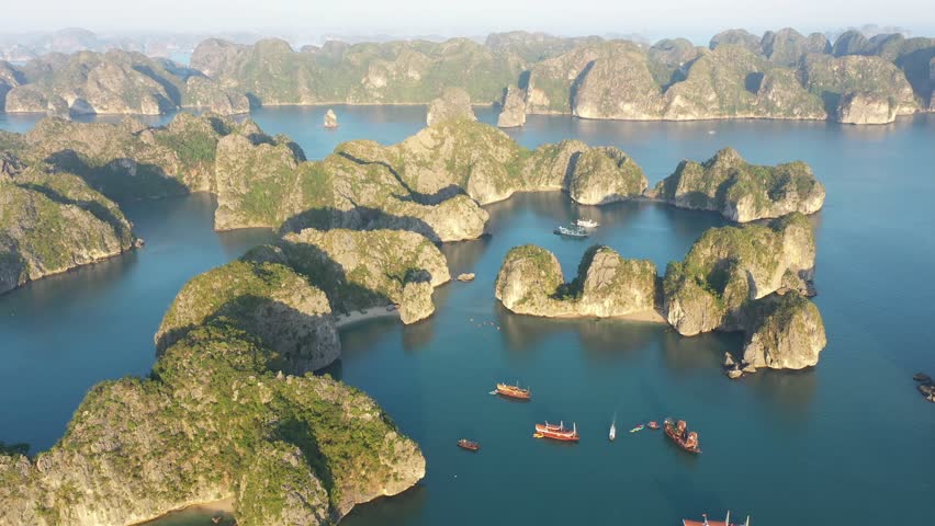 Limestone karst islands of Ha Long Bay rising from tranquil turquoise waters, featuring tourist boats gliding across scenic Vietnamese seascape under sunny summer sky