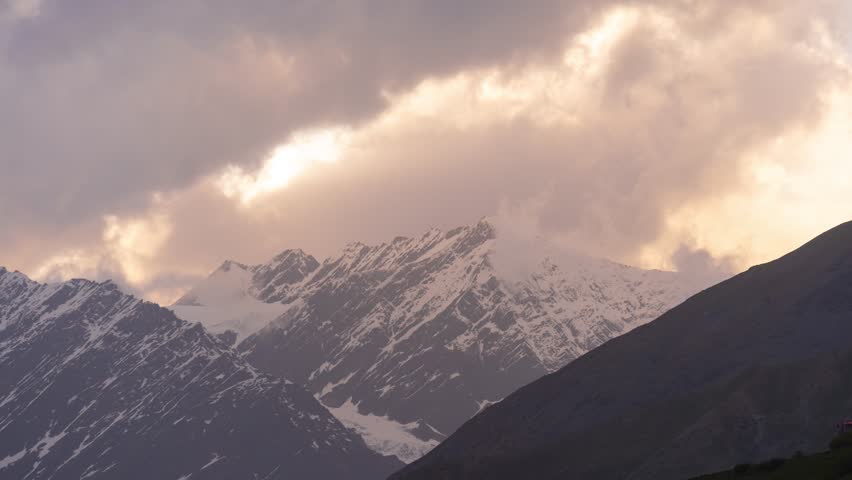 4K Zoom In Time-lapse shot of sunrays in front of snowy Himalayan mountain peak covered by clouds during the sunset at Lahaul Valley in Himachal Pradesh, India. Sun beam during the sunset in Himalayas