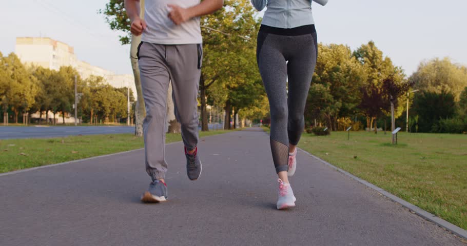 Legs of fit active couple running on sidewalk in summer park. Runners in sportswear and sport shoes jogging together on trail, two athletes training muscular endurance with physical exercises