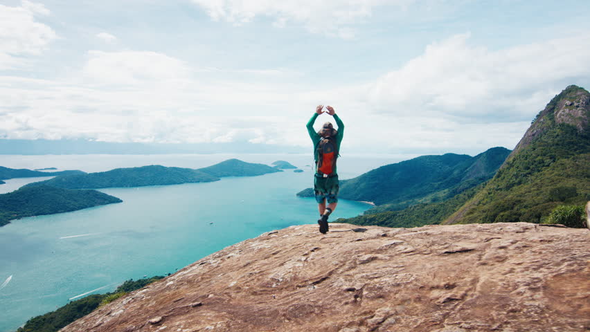 Adult male hiker celebrates reaching the top by extending his hands on top the mountain in Brazil
