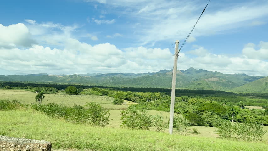 A lush landscape at Vinales National Park, Cuba  with palm trees and mountains, under a bright sky with a few clouds, tc01