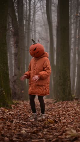 Girl in orange jacket with a spooky carved pumpkin head dancing on Halloween in the misty autumn forest. Fall holiday concept