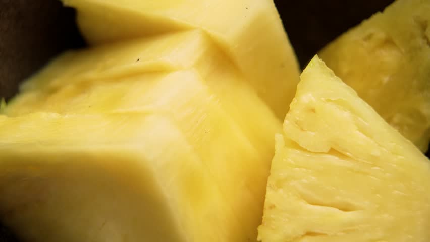 Fresh yellow pineapple slices in a dark ceramic bowl. Macro shot. Rotation