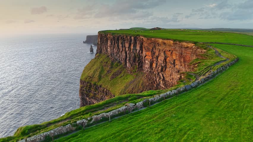 Flying over green grass near the edge of Cliff of Moher - one of the most popular tourist destinations in Ireland. Aerial breathtaking cliffs of Moher in Ireland, County Clare