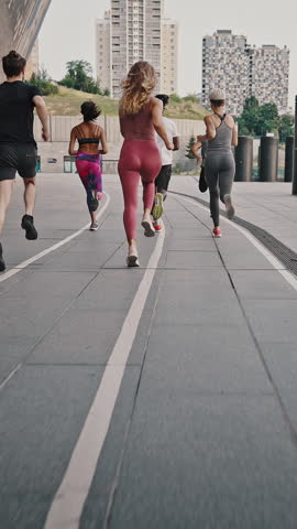 Back view of big team of athletes has a group training session on the urban streets of a big city. A group of people jogging together at sunrise.