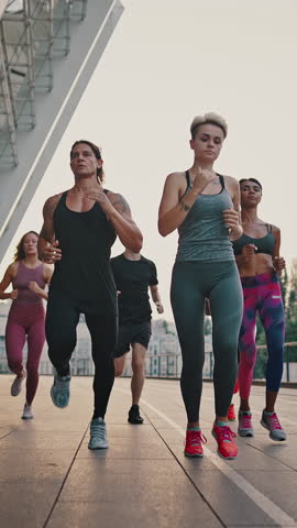 Running club. Multiracial team of like-minded people running through the city streets. People in sports uniforms and shoes have a group workout.