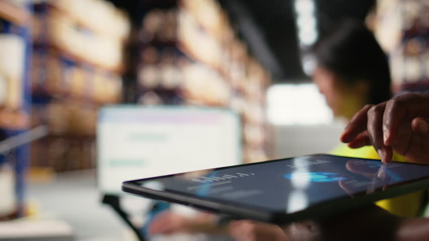 Close up of african american person checking tracking info for parcels on tablet, ensuring correct shipment address for express delivery services in warehouse. AWB distribution numbers. Camera A.