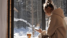 Woman wrapped in blanket sits by window using smartphone surrounded by forest calm and soft light Scene reflects how online habits shape quiet moments Online presence online moment merge gently - Powered by Shutterstock - Get 15% off with code: PIKWIZARD15