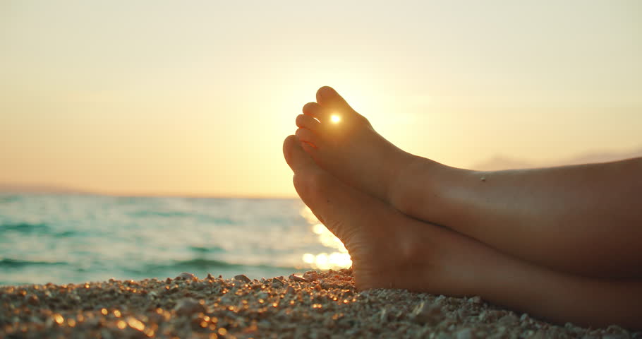 Feet of woman resting on pebbled beach during golden sunset on summer vacations