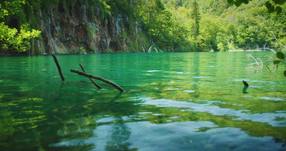 Emerald green lake reflecting cliffside forest under summer light in Plitvice National Park Croatia